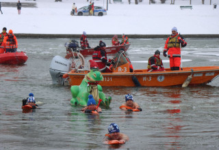 Uczestnicy wydarzenia Przeciągnij Smoka przez Wisłę płyną w zimnej wodzie pod opieką ratowników WOPR